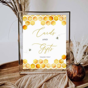 May include: A framed sign with a watercolor honeycomb design in shades of yellow and orange. The sign reads "Cards and Gifts" in elegant gold script, with two small bee illustrations. The words "Thank You!" are at the bottom.