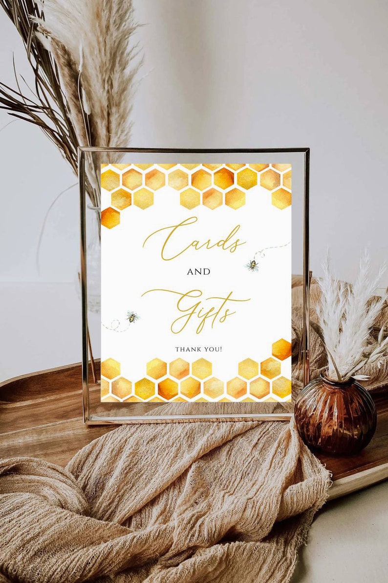 May include: A framed sign with a watercolor honeycomb design in shades of yellow and orange. The sign reads "Cards and Gifts" in elegant gold script, with two small bee illustrations. The words "Thank You!" are at the bottom.