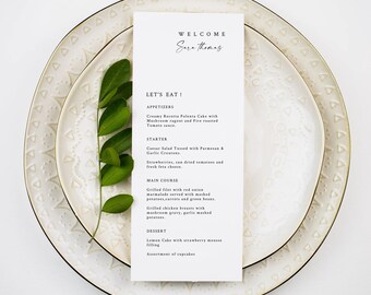 Puede incluir: Una tarjeta de menú blanca con texto negro sobre fondo blanco. La tarjeta de menú se titula "Let's Eat!" y enumera aperitivos, un entrante, un plato principal y un postre. La tarjeta de menú se coloca encima de dos platos blancos con un borde dorado.