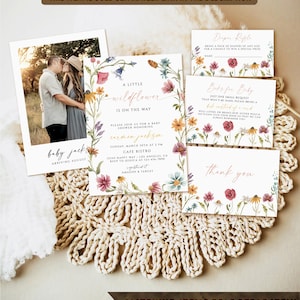 K&ouml;nnte beinhalten: Ein Satz druckbarer Babyparty-Einladungen mit einem floralen Design. Die Einladungen zeigen eine Aquarell-Illustration von Wildblumen in Rosa-, Gelb- und Blaut&ouml;nen. Der Text auf den Einladungen lautet "Eine kleine Wildblume ist unterwegs" und enth&auml;lt Details zur Babyparty, wie Datum, Uhrzeit und Ort. Die Einladungen beinhalten auch eine Dankeskarte und eine Windel-Tombola-Karte.