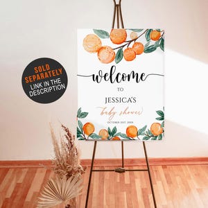 May include: A welcome sign for Jessica's baby shower, featuring orange watercolor illustrations and the text "welcome to Jessica's baby shower October 21st, 20XX". The sign is displayed on a dark brown easel.