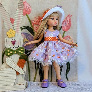 May include: A doll wearing a lavender dress with a white lace trim, a white hat with a red and white band, and purple shoes. A wooden Easter bunny with a carrot stands beside the doll. The dress has a bunny and carrot pattern.