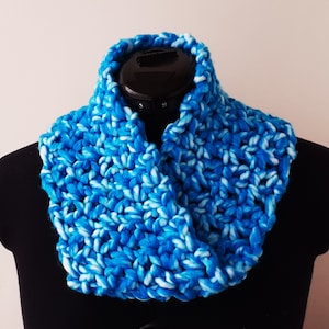 Op de afbeelding: Een blauwe en witte gecrochete oneindige sjaal. De sjaal is gemaakt met een dik garen en heeft een losse, open structuur.