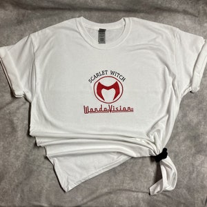 May include: White t-shirt with a red embroidered logo that says "Scarlet Witch WandaVision" with a stylised "M" inside a circle.