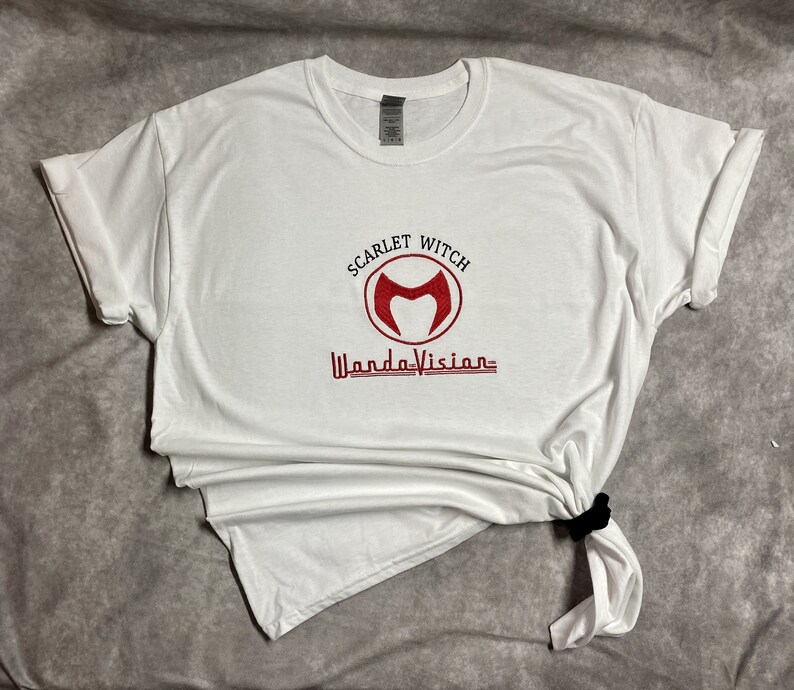 May include: White t-shirt with a red embroidered logo that says "Scarlet Witch WandaVision" with a stylised "M" inside a circle.