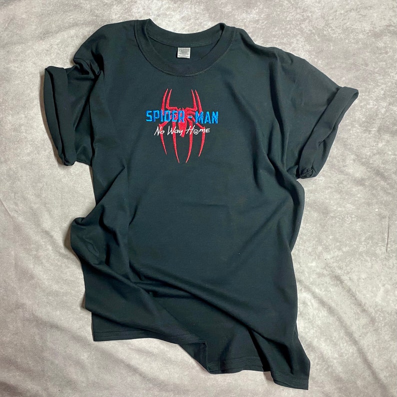 以下が含まれることがあります： 赤い糸と青い糸で刺繍されたスパイダーマンのロゴと「スパイダーマン ノー・ウェイ・ホーム」の文字が書かれた黒いTシャツ。