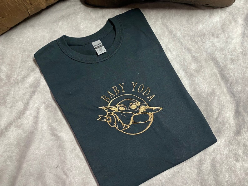 May include: Black t-shirt with a gold embroidered image of Baby Yoda, surrounded by a circle with the text "BABY YODA".