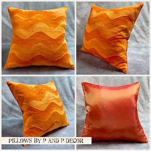 K&ouml;nnte beinhalten: Vier dekorative Kissen, zwei in leuchtendem Orange mit einem wellenf&ouml;rmigen Muster und zwei in einfarbiger orange-roter Farbe. Die Kissen sind in einem Raster auf einer hellgrauen Oberfl&auml;che angeordnet. Der Text "PILLOWS BY P AND P DECOR" ist am unteren Rand des Bildes gedruckt.