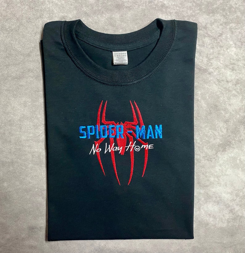 以下が含まれることがあります： 赤い糸と青い糸で刺繍されたスパイダーマンのロゴと「No Way Home」の文字が書かれた黒いTシャツ。