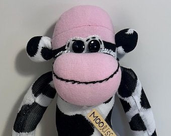 May include: A handmade sock monkey in a cow design. The plush toy features a pink head, muzzle, and feet, with black and white spotted body and limbs. The tag reads "Moolissa".
