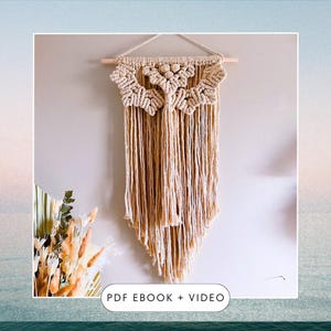 May include: A beige macrame wall hanging with a geometric pattern and fringe. The hanging is attached to a wooden dowel rod. "PDF EBOOK + VIDEO" is written in black text at the bottom of the image.