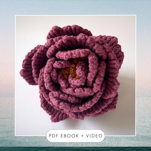 以下が含まれることがあります： 濃いワインレッドのクロシェ編み花をクローズアップした写真。花の中心は薄い茶色の糸でできています。画像には「PDF EBOOK + VIDEO」というテキストが含まれています。