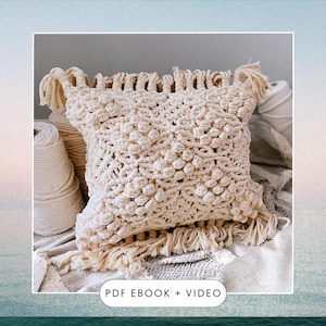 Könnte beinhalten: Ein cremefarbenes Makramee-Kissen mit einem strukturierten, geknüpften Design und Fransenbesatz. Das Kissen liegt auf einer cremefarbenen Stoffoberfläche. "PDF EBOOK + VIDEO" steht in schwarzer Schrift am unteren Rand des Bildes.