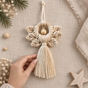 May include: A macrame angel ornament crafted from off-white cotton cord, featuring a circular wooden ring head, a smooth wooden bead, and intricate knotted wing patterns. The lower section consists of a long, flowing fringe tassel.