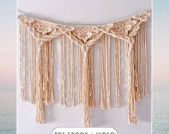 May include: A macrame wall hanging with a cream colored, geometric design. The hanging has a series of tassels along the bottom. The text "PDF EBOOK + VIDEO" is at the bottom of the image.