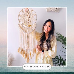 May include: A woman holds up a large, beige macrame dreamcatcher with a starburst design. The dreamcatcher has a wooden hoop and is decorated with tassels. The text "PDF EBOOK + VIDEO" is at the bottom of the image.