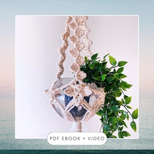May include: A macrame plant hanger with a white cord and a glass globe. The hanger is holding a small green plant. The text "PDF EBOOK + VIDEO" is at the bottom of the image.