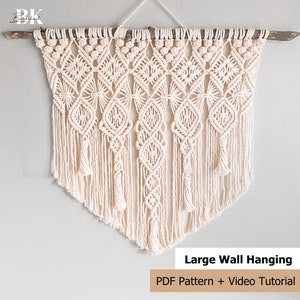 Pu&ograve; includere: Un grande arazzo da parete in macram&egrave; con un motivo geometrico di colore crema. L'arazzo &egrave; realizzato con cordoncino di cotone e ha un'asta di legno nella parte superiore. Il testo "Large Wall Hanging" e "PDF Pattern + Video Tutorial" &egrave; nella parte inferiore dell'immagine.