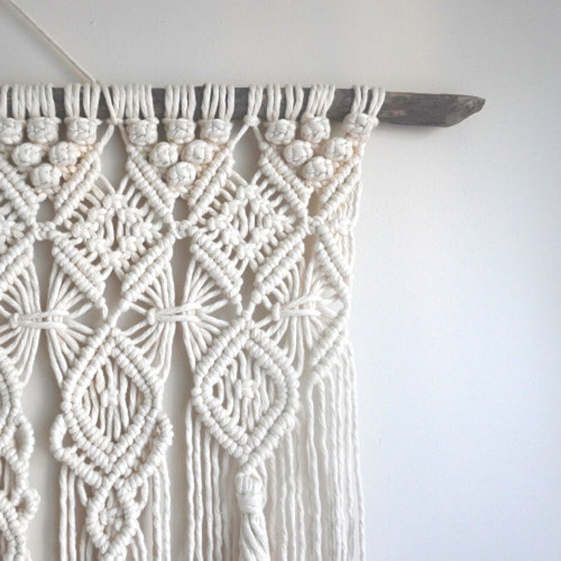 Pu&ograve; includere: Arazzo da parete in macram&egrave; bianco con un motivo geometrico. L'arazzo &egrave; realizzato con cordoncino di cotone ed &egrave; fissato a un bastone di legno.