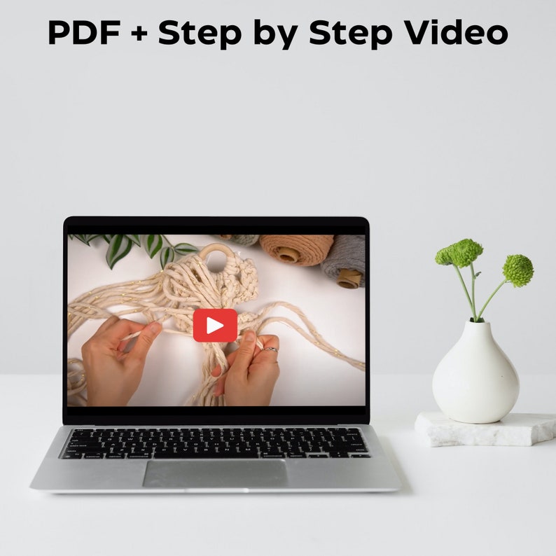 Pu&ograve; includere: Lo schermo di un laptop mostra un tutorial video su come realizzare un'appeso da parete in macram&egrave;. Il video mostra le mani di una persona che fa nodi con una corda di colore naturale. Il testo "PDF + Step by Step Video" &egrave; visualizzato nella parte superiore dello schermo.