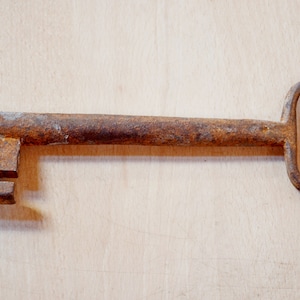 May include: A rusty metal key with a large, flat head and a rounded loop at the end.