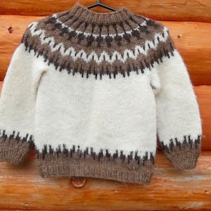 May include: A white and brown knitted sweater with a traditional Scandinavian pattern. The sweater has a high neck and long sleeves.
