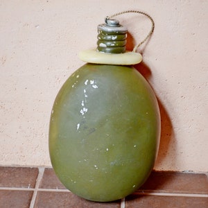 May include: A green metal canteen with a white plastic cap and a brown cord.