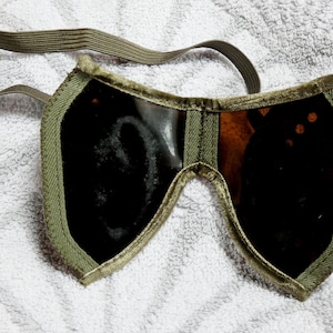 Peut inclure: Protection oculaire vintage avec des verres foncés et une sangle élastique vert kaki. Le couvre-œil est encadré d'un tissu vert assorti. Les verres semblent être faits d'un matériau foncé, peut-être teinté.