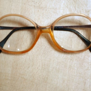 May include: A pair of round, amber-colored eyeglasses with black arms.