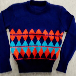 Pode incluir: Um suéter azul marinho com um padrão geométrico em laranja, turquesa e vermelho.