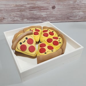 May include: A white square tray holds six slices of pizza. Each slice has a yellow base, red pepperoni, and a brown crust. The pizza slices have smiling faces. The tray sits on a light gray surface.