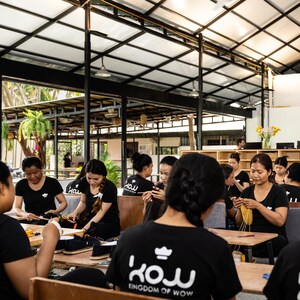 A group of women wearing black shirts with the logo "KINGDOM OF WOW" are working on crochet slippers