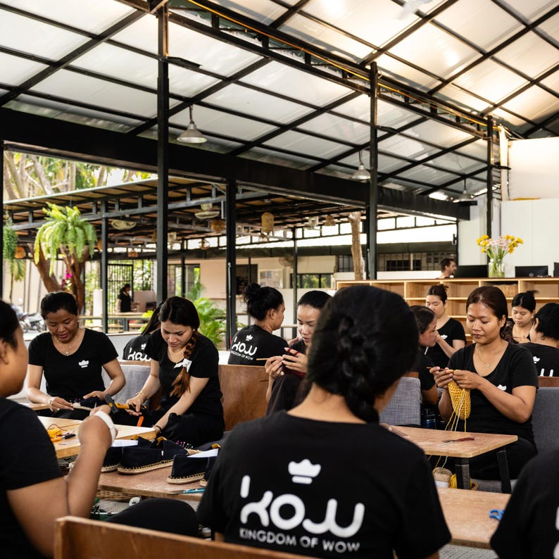 A group of women wearing black shirts with the logo "KINGDOM OF WOW" are working on crochet slippers