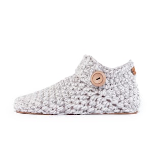 Side angle of a beige off-white wool slipper with wooden button fastening and suede leather sole. Hand-knitted by Kingdom of Wow. Barefoot design for Men and Women.