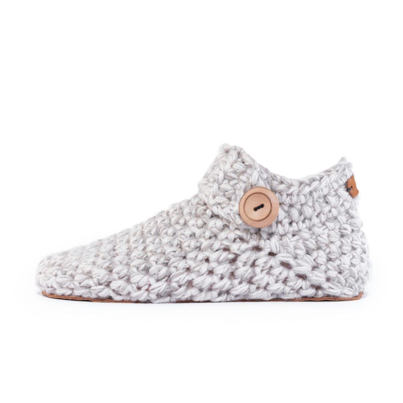 Side angle of a beige off-white wool slipper with wooden button fastening and suede leather sole. Hand-knitted by Kingdom of Wow. Barefoot design for Men and Women.