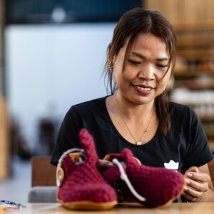 A woman is carefully inspecting a pair of handmade red knitted slippers. The shoes have a unique design and are made with high-quality materials.