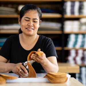 Smiling lady punches holes in handmade leather soles for woolen slippers at Kingdom of Wow workshop