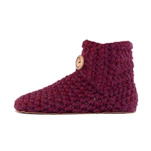 A mulberry red hand knitted slipper boot with a wooden button closure. The slipper has a thick, textured knit and a leather sole. Barefoot slippers for indoor use. Warm, cozy and comfortable. Perfect loungewear.