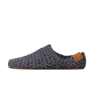 A single dark gray slipper with a textured, crocheted design. The slipper has a rounded toe and a small, brown leather tag on the heel. The sole is made of suede leather. Barefoot flexible design.