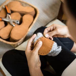 Woman hand sews a leather sole on a woolen upper to create comfortable indoor slipper