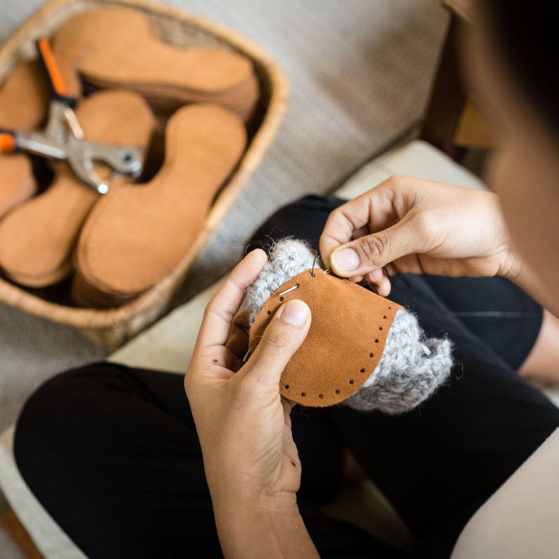 Woman hand sews a leather sole on a woolen upper to create comfortable indoor slipper