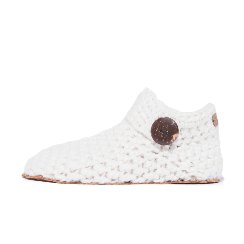 Side angle of a white wool slipper with wooden button fastening and suede leather sole. Handmade by Kingdom of Wow. Barefoot design for Men and Women.