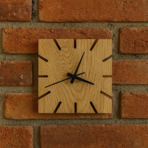 Peut inclure: Horloge murale carrée en bois clair. L'horloge a des aiguilles noires et des repères noirs indiquant les heures. L'horloge est fixée sur un mur de briques rouges.