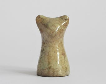 May include: A small, upright ceramic sculpture with a smooth, glossy finish. The object features a light beige and tan color palette with a distinct, dark brown crackle glaze pattern covering the entire surface. It has a curved, hourglass-like shape.