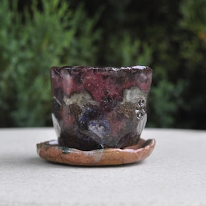 Small ceramic brown planter with gray and blue smears.The saucer is warm light brown with green smears. Raku pottery.