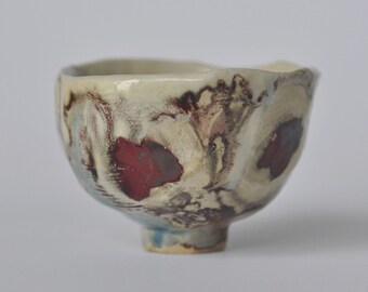 Asymmetrical raku pottery chawan with a brown-red, blue and grey smear.