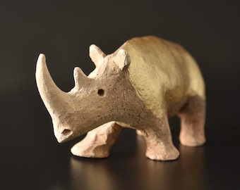 Puede incluir: Una figura de rinoceronte hecha de un material de arcilla texturizada de color marrón claro. La escultura animal presenta un cuerno prominente en el hocico y un acabado dorado metálico distintivo que cubre la parte superior del lomo y la grupa.
