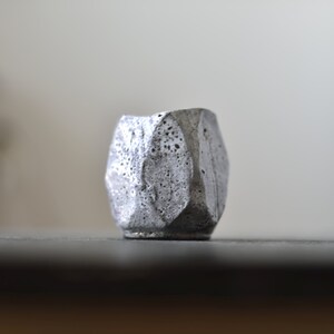 May include: A small, gray, geometric planter with a rough, textured surface.