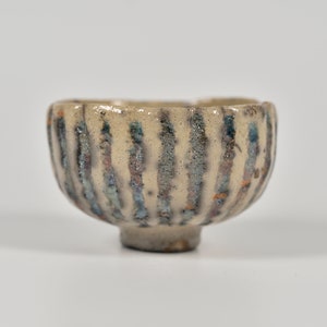 May include: A small, white ceramic bowl with a textured, striped design in shades of blue and brown. The bowl has a rounded shape and a small foot.