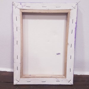 May include: Back of a rectangular canvas art piece. The canvas is stretched over a wooden frame and secured with staples. The edges are painted purple. The canvas is white and shows a few small marks.